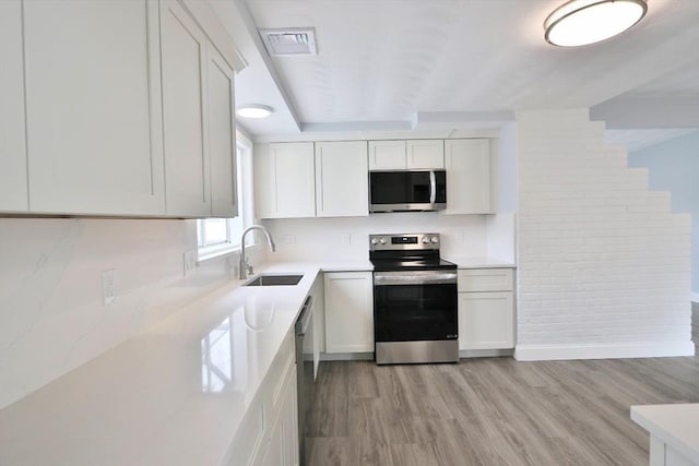 kitchen with appliances with stainless steel finishes, a sink, light wood-type flooring, and white cabinets