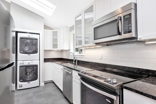 kitchen featuring stainless steel appliances, stacked washing machine and dryer, a sink, a skylight, and vaulted ceiling