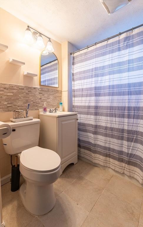 bathroom featuring tile walls, a shower with shower curtain, a textured ceiling, tile patterned floors, and toilet