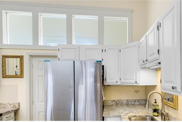 kitchen with white cabinets, stainless steel fridge, light stone counters, and sink