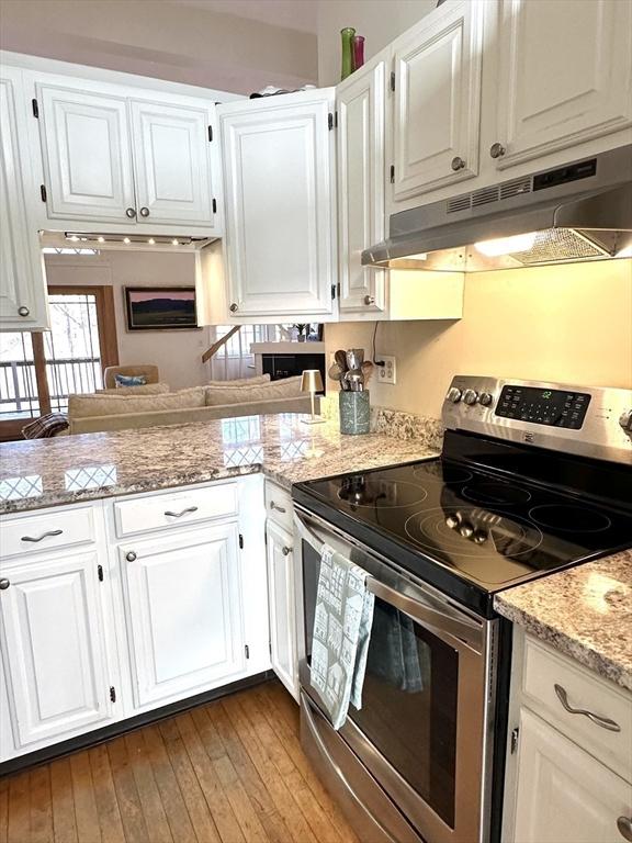 kitchen with wood-type flooring, kitchen peninsula, light stone countertops, stainless steel electric range oven, and white cabinetry