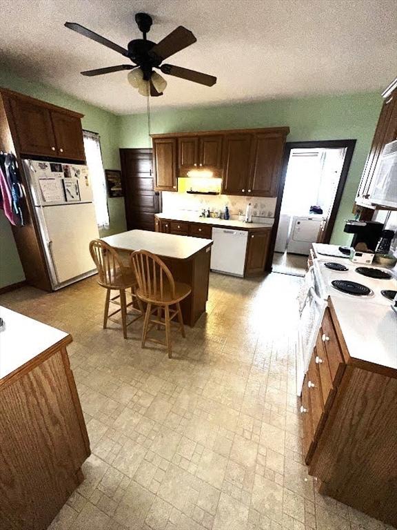 kitchen with a ceiling fan, a textured ceiling, white appliances, light countertops, and a kitchen island
