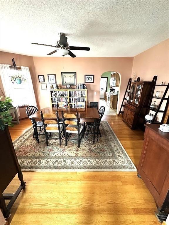 dining area featuring wood finished floors, arched walkways, a textured ceiling, and ceiling fan
