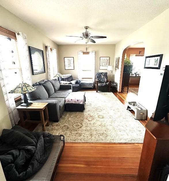 living area featuring arched walkways, wood finished floors, and ceiling fan