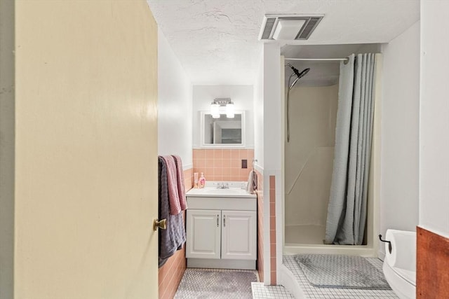 full bathroom featuring a textured ceiling, vanity, visible vents, tile walls, and a stall shower