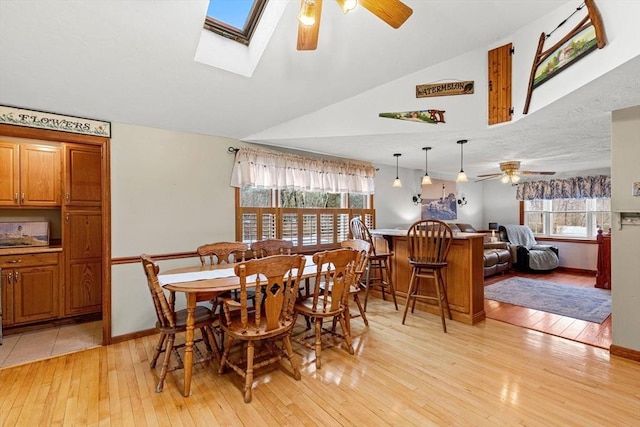 dining area featuring light wood-type flooring, vaulted ceiling with skylight, baseboards, and ceiling fan