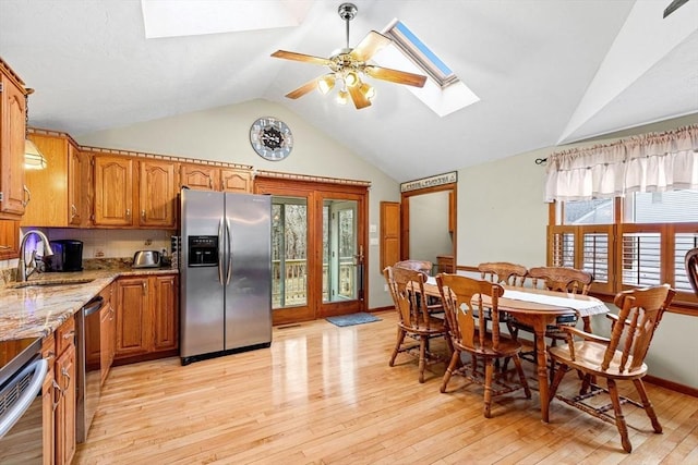 kitchen featuring light wood finished floors, light stone counters, brown cabinets, stainless steel appliances, and a sink