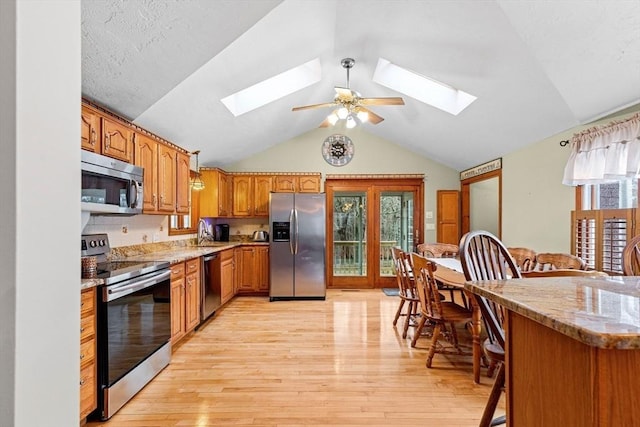 kitchen with stainless steel appliances, light wood finished floors, brown cabinetry, and a sink