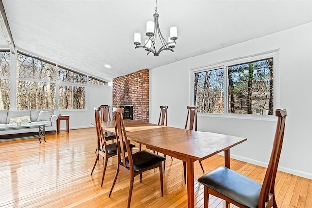 dining area with lofted ceiling, a fireplace, a chandelier, and light hardwood / wood-style flooring