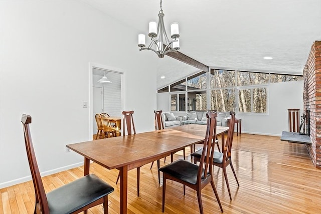 dining space featuring lofted ceiling with beams, a chandelier, a fireplace, and light wood-type flooring