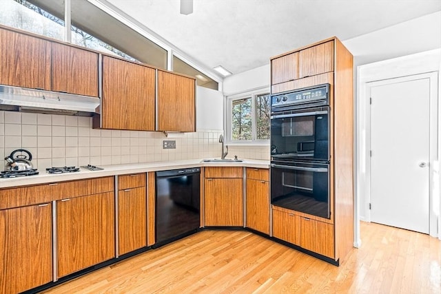 kitchen featuring lofted ceiling, sink, tasteful backsplash, light hardwood / wood-style flooring, and black appliances