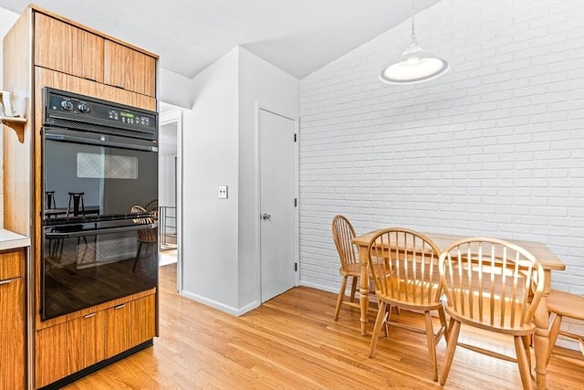 kitchen with lofted ceiling, double oven, pendant lighting, brick wall, and light hardwood / wood-style floors