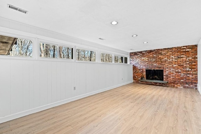 unfurnished living room featuring brick wall, light hardwood / wood-style floors, and a brick fireplace