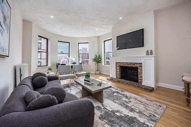 living area with wood finished floors, baseboards, a brick fireplace, and recessed lighting