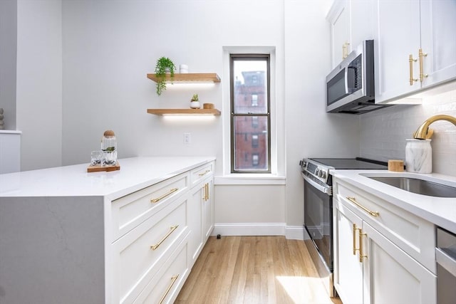 kitchen featuring light wood-style flooring, tasteful backsplash, appliances with stainless steel finishes, light countertops, and a sink