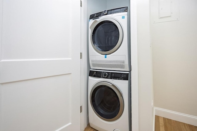 laundry area with stacked washer / dryer, light wood-style floors, and baseboards