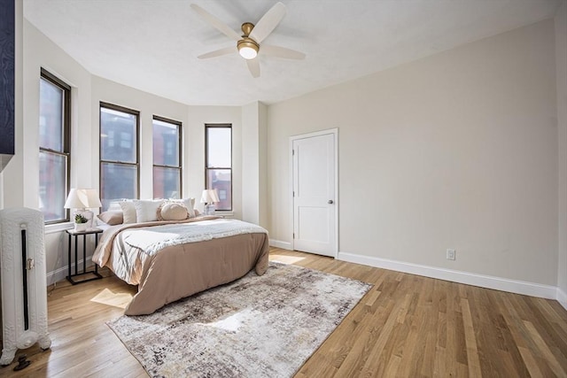 bedroom featuring light wood-style flooring, radiator, baseboards, and multiple windows