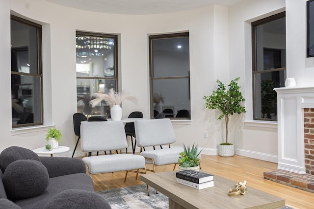 living area featuring a brick fireplace, baseboards, and wood finished floors