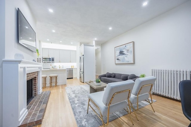 living room with radiator heating unit, a fireplace, light wood-style floors, and recessed lighting