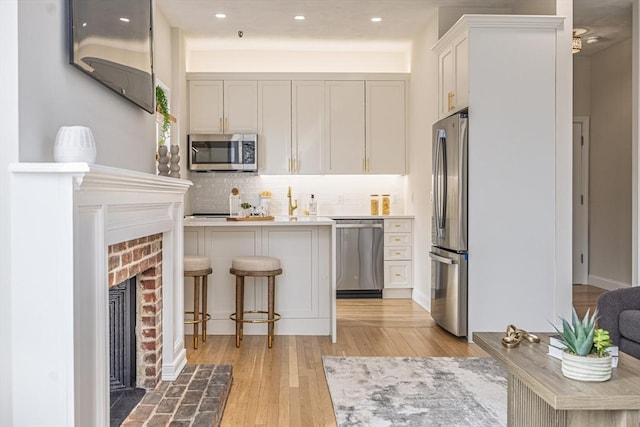 kitchen with light countertops, backsplash, light wood-style floors, a breakfast bar area, and stainless steel appliances