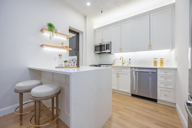 kitchen featuring tasteful backsplash, a breakfast bar, a peninsula, light wood-style flooring, and stainless steel appliances