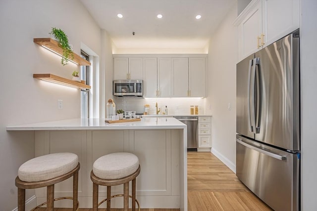 kitchen with a peninsula, open shelves, white cabinetry, appliances with stainless steel finishes, and light countertops