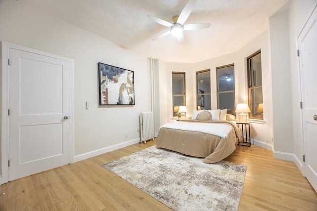 bedroom featuring light wood finished floors, ceiling fan, radiator heating unit, and baseboards