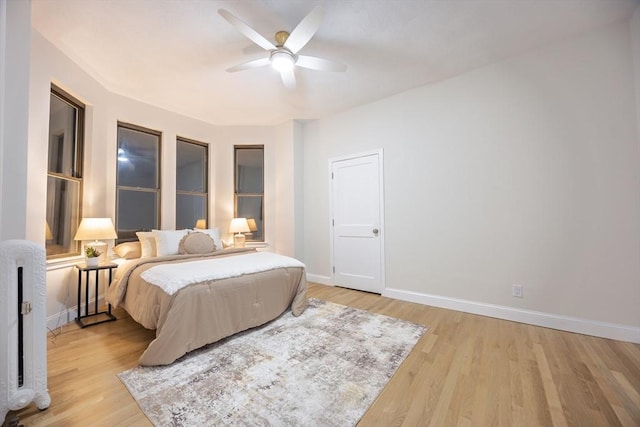 bedroom with ceiling fan, radiator heating unit, light wood finished floors, and baseboards