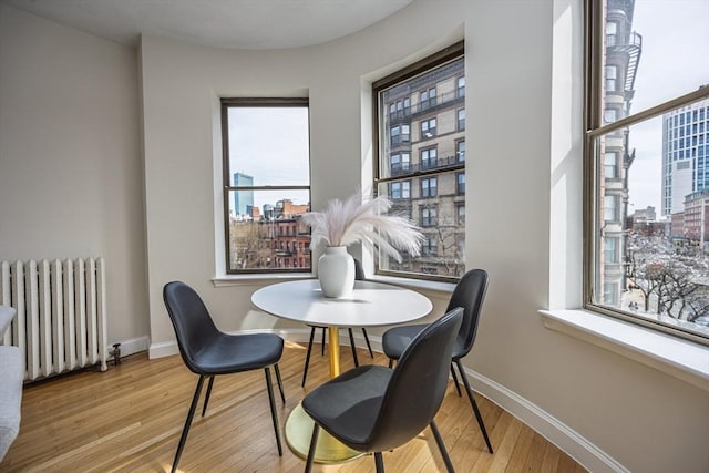 dining room with radiator heating unit, a view of city, light wood finished floors, and baseboards