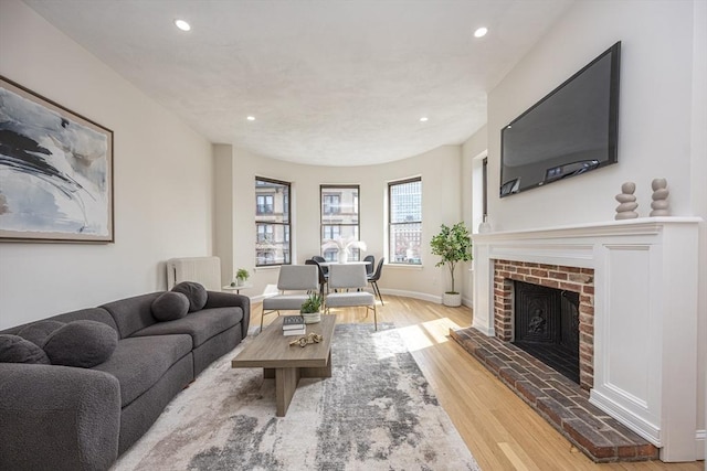 living room featuring wood finished floors, baseboards, a brick fireplace, and recessed lighting