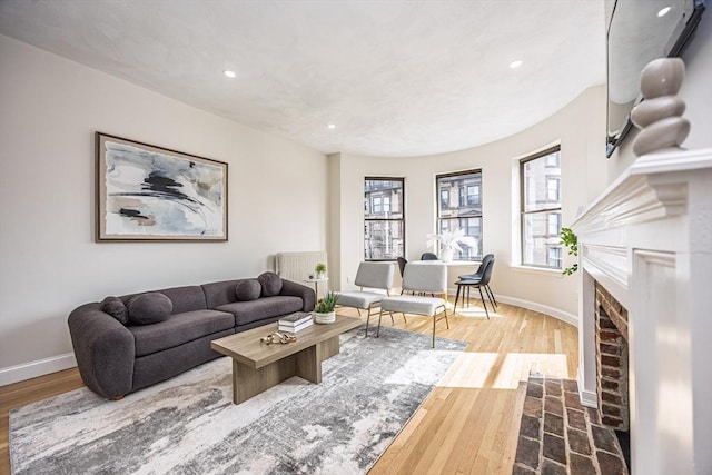 living room featuring wood finished floors, baseboards, a brick fireplace, and recessed lighting