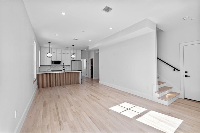 unfurnished living room with light wood finished floors, stairs, baseboards, and visible vents