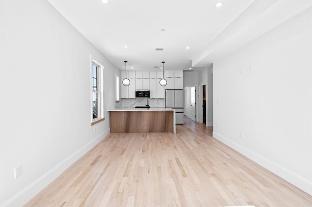 kitchen with stainless steel microwave, fridge, light wood finished floors, open floor plan, and light countertops