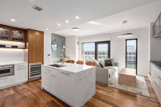 kitchen with white cabinetry, an island with sink, sink, light stone counters, and wall oven