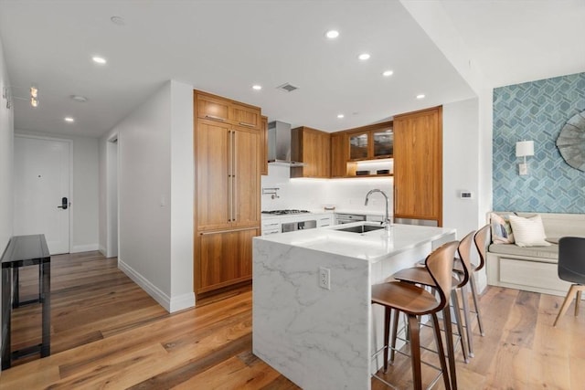 kitchen with white gas stovetop, sink, a kitchen bar, light stone countertops, and light hardwood / wood-style flooring