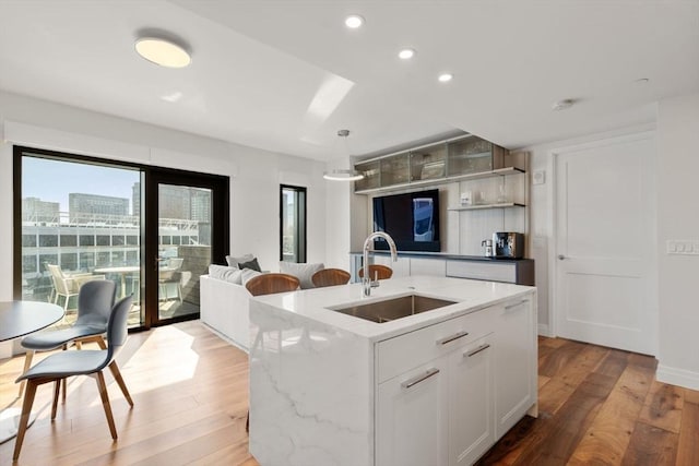 kitchen featuring pendant lighting, white cabinetry, sink, a kitchen island with sink, and light stone counters