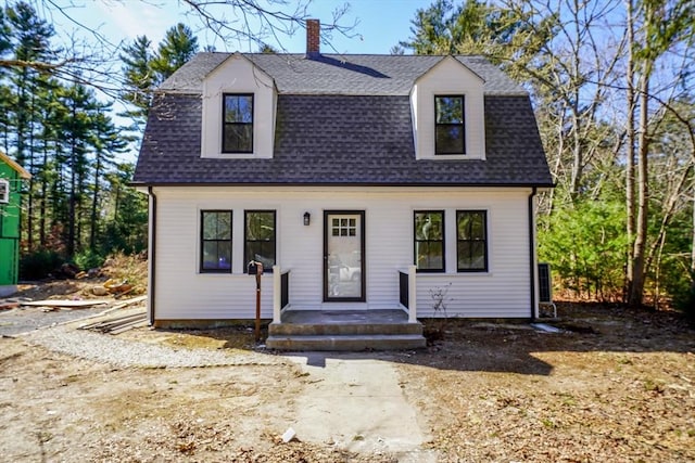 colonial inspired home featuring a gambrel roof, a chimney, and roof with shingles