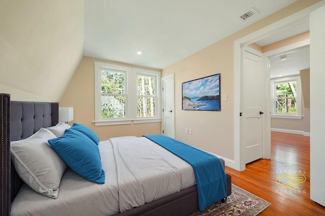 bedroom with visible vents, baseboards, lofted ceiling, and wood finished floors