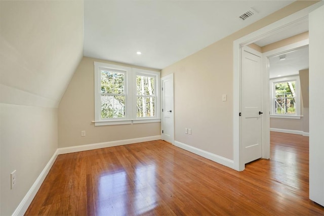 additional living space with visible vents, wood finished floors, baseboards, and vaulted ceiling