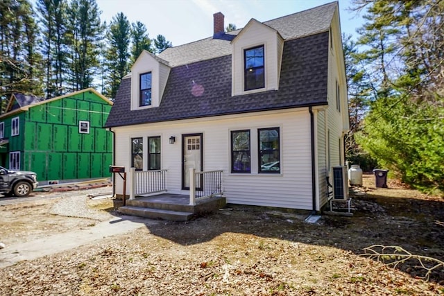 dutch colonial featuring a gambrel roof, a chimney, and roof with shingles