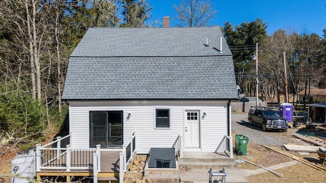 view of front facade with a deck, roof with shingles, and a chimney