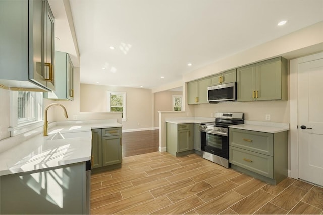 kitchen featuring wood finish floors, light countertops, a peninsula, stainless steel appliances, and green cabinetry