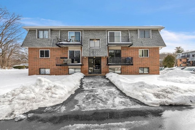 view of front of house with a balcony, a shingled roof, and brick siding