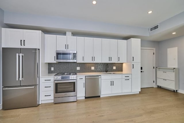 kitchen with appliances with stainless steel finishes, a sink, light countertops, recessed lighting, and white cabinetry