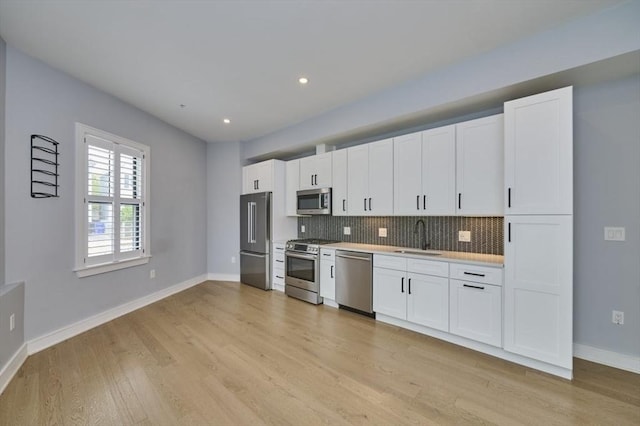kitchen featuring appliances with stainless steel finishes, a sink, backsplash, light countertops, and light wood-style flooring