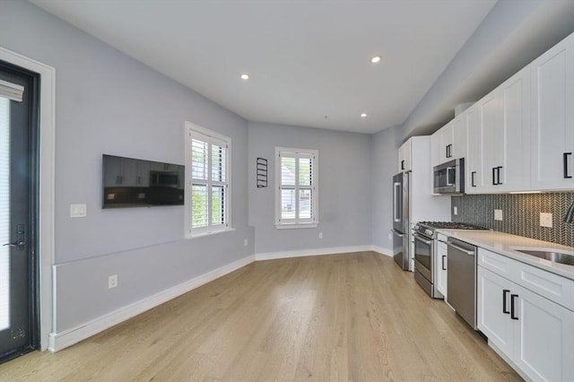 kitchen featuring appliances with stainless steel finishes, light wood-type flooring, a sink, decorative backsplash, and white cabinetry