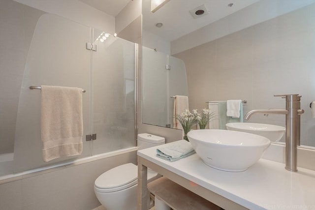 bathroom featuring toilet, enclosed tub / shower combo, vanity, and tile walls