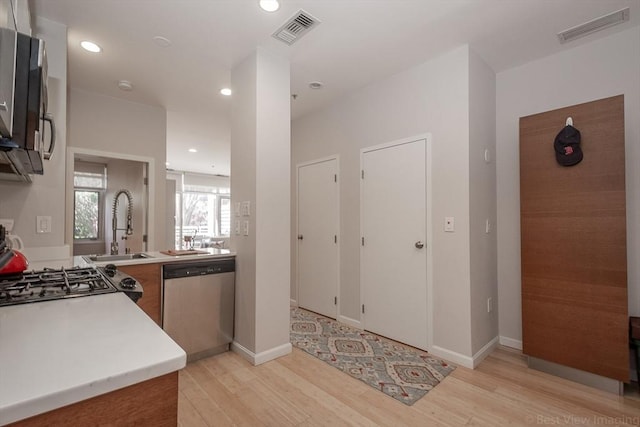 kitchen with appliances with stainless steel finishes, light wood-style flooring, a sink, light countertops, and recessed lighting
