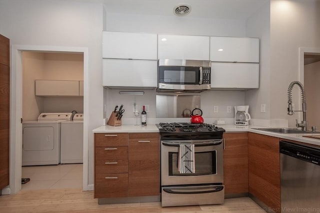 kitchen featuring appliances with stainless steel finishes, washer and clothes dryer, a sink, brown cabinets, and white cabinets