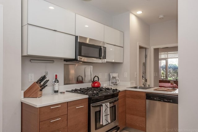 kitchen featuring appliances with stainless steel finishes, white cabinets, a sink, light countertops, and brown cabinets